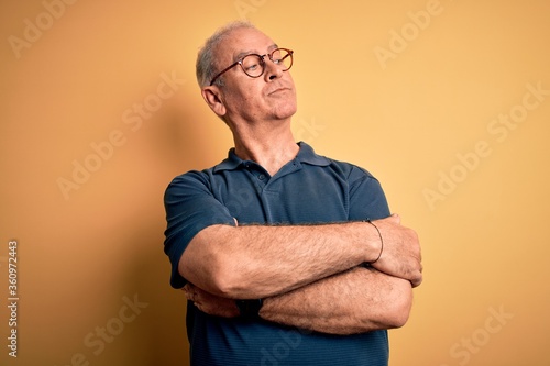 Middle age handsome hoary man wearing casual polo and glasses over yellow background looking to the side with arms crossed convinced and confident © Krakenimages.com