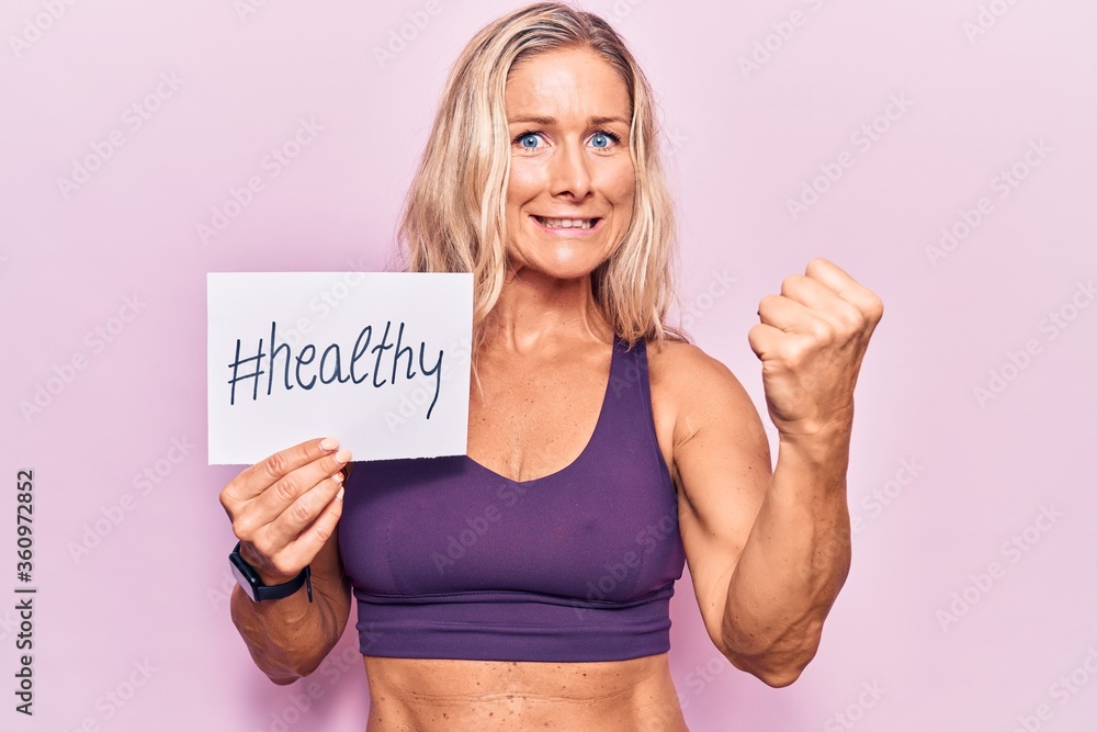 Middle age caucasian blonde woman wearing sportswear holding healthy banner annoyed and frustrated shouting with anger, yelling crazy with anger and hand raised Middle age caucasian blonde woman wearing sportswear holding healthy banner annoyed and frustrated shouting with anger, yelling crazy with anger and hand raised