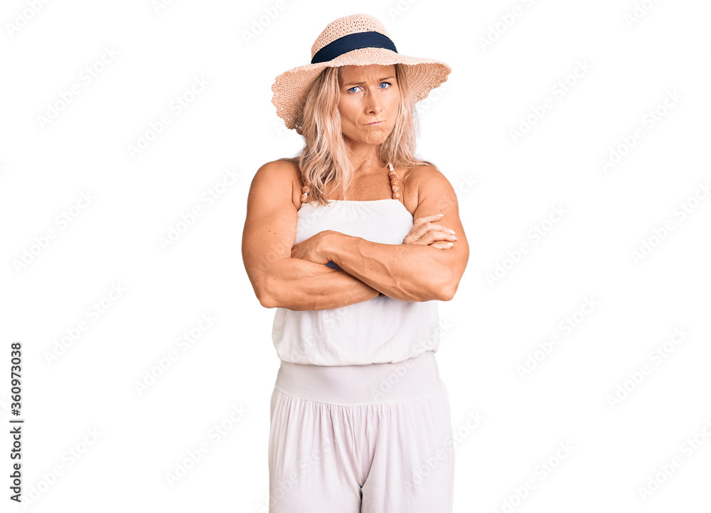 Middle age fit blonde woman wearing summer hat skeptic and nervous, disapproving expression on face with crossed arms. negative person. Middle age fit blonde woman wearing summer hat skeptic and nervous, disapproving expression on face with crossed arms. negative person.