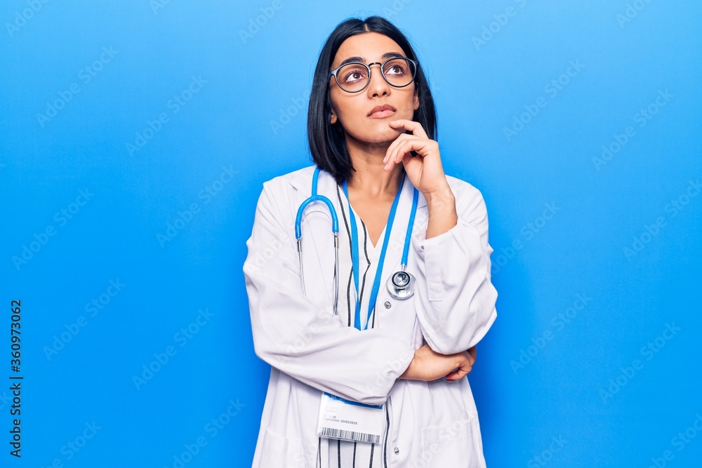 Young beautiful latin woman wearing doctor stethoscope and id card serious face thinking about question with hand on chin, thoughtful about confusing idea Young beautiful latin woman wearing doctor stethoscope and id card serious face thinking about question with hand on chin, thoughtful about confusing idea