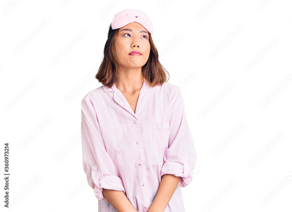 Young beautiful chinese girl wearing sleep mask and pajama smiling looking to the side and staring away thinking. Young beautiful chinese girl wearing sleep mask and pajama smiling looking to the side and staring away thinking.