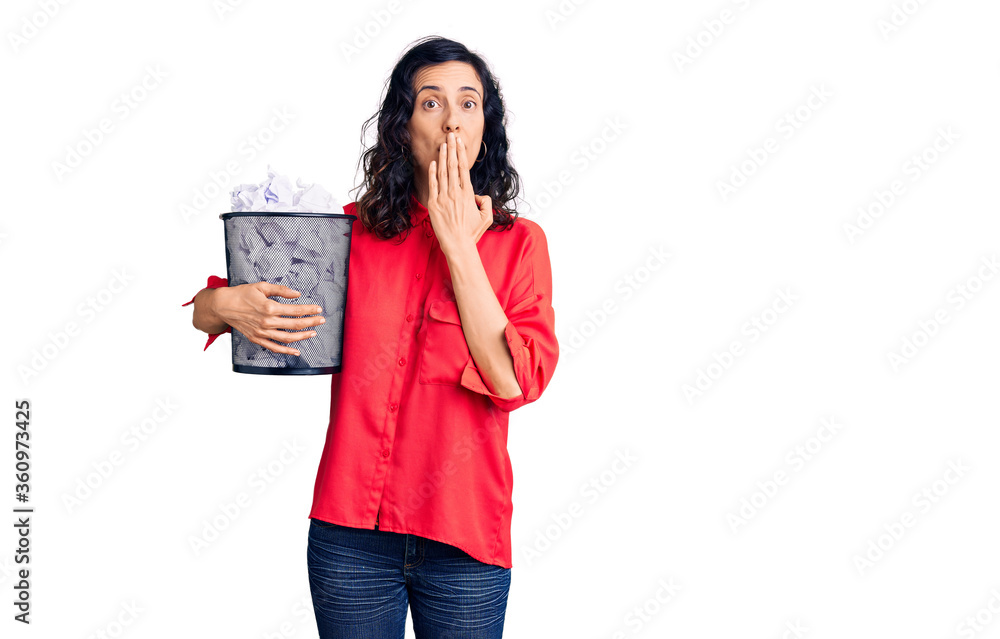 Young beautiful hispanic woman holding paper bin full of crumpled papers covering mouth with hand, shocked and afraid for mistake. surprised expression Young beautiful hispanic woman holding paper bin full of crumpled papers covering mouth with hand, shocked and afraid for mistake. surprised expression