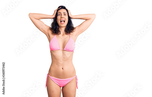 Young beautiful hispanic woman wearing bikini crazy and scared with hands on head, afraid and surprised of shock with open mouth