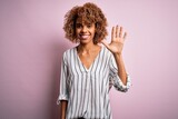 Beautiful african american woman with curly hair wearing striped t-shirt over pink background showing and pointing up with fingers number five while smiling confident and happy.