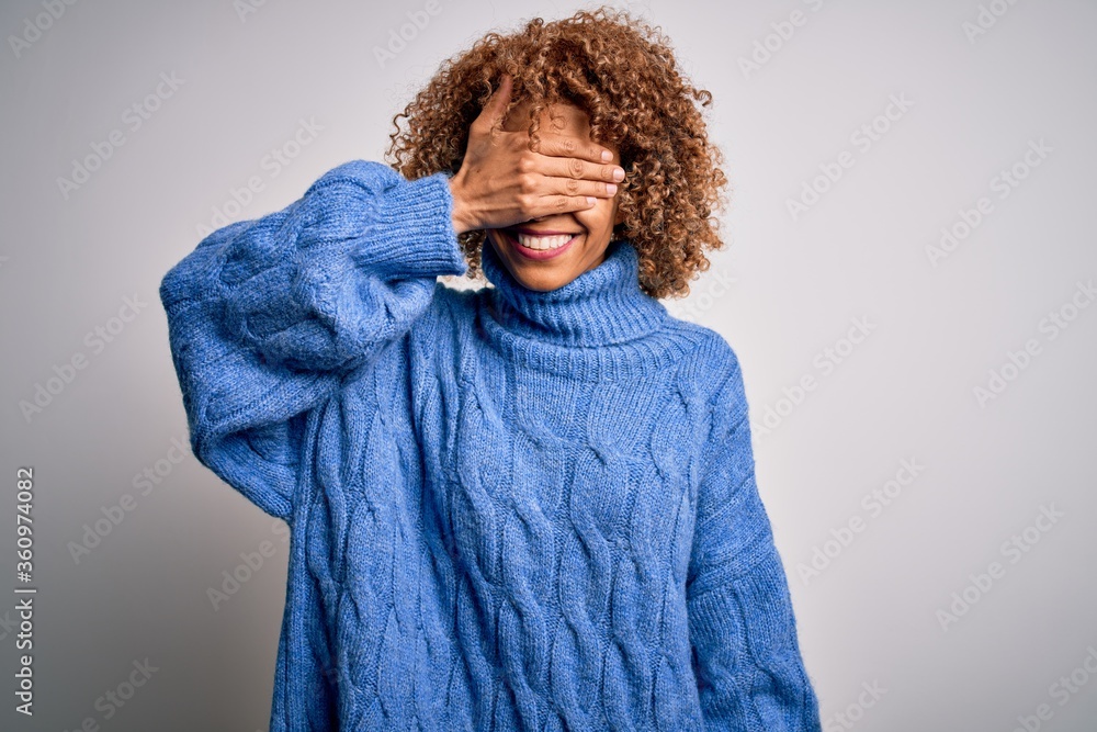 Young beautiful african american woman wearing turtleneck sweater over white background smiling and laughing with hand on face covering eyes for surprise. Blind concept. Young beautiful african american woman wearing turtleneck sweater over white background smiling and laughing with hand on face covering eyes for surprise. Blind concept.
