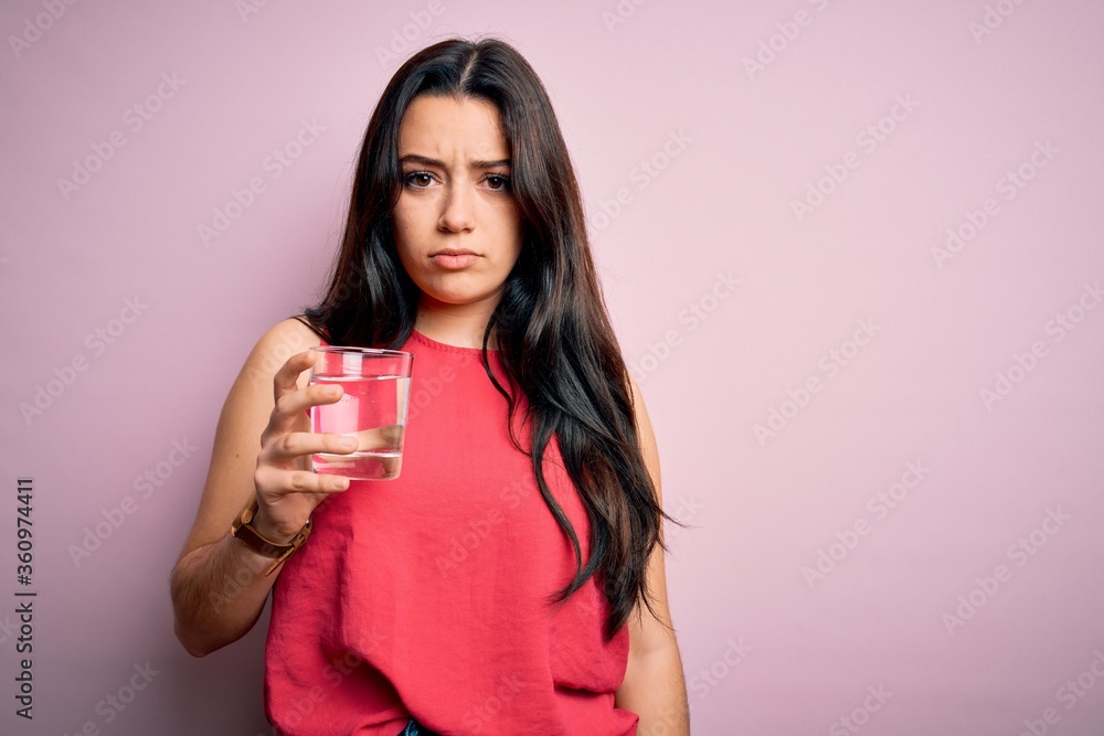 Young brunette woman drinking a glass of fresh water over pink isolated background with a confident expression on smart face thinking serious Young brunette woman drinking a glass of fresh water over pink isolated background with a confident expression on smart face thinking serious