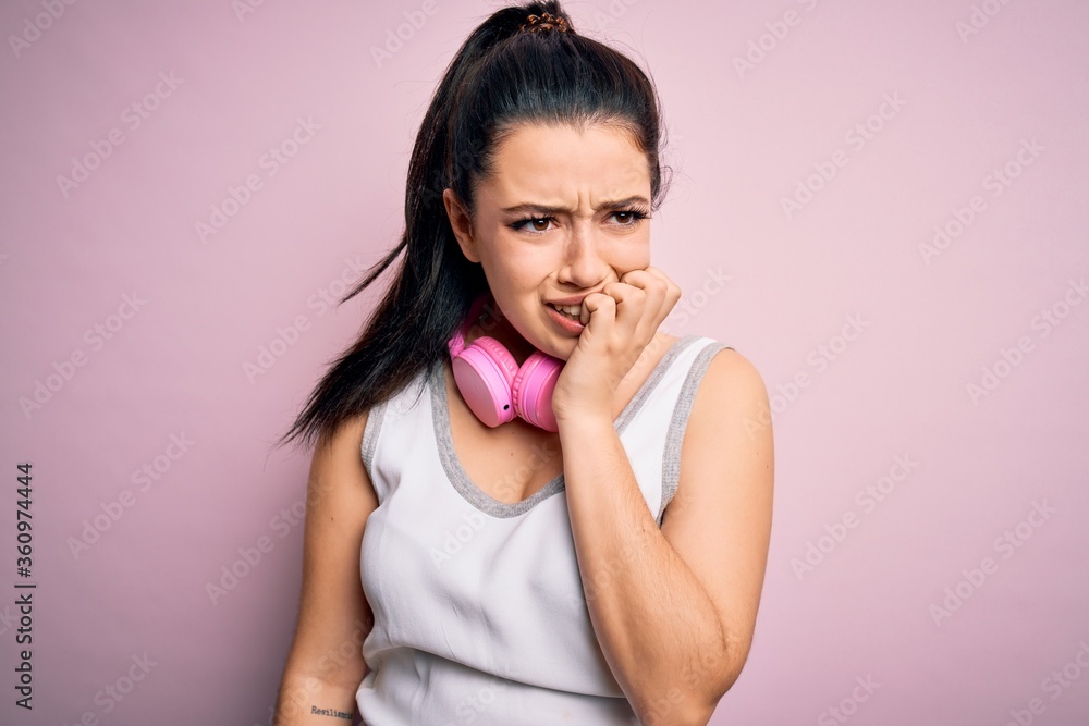 Young brunette fitness woman wearing gym headphones over pink isolated background looking stressed and nervous with hands on mouth biting nails. Anxiety problem. Young brunette fitness woman wearing gym headphones over pink isolated background looking stressed and nervous with hands on mouth biting nails. Anxiety problem.