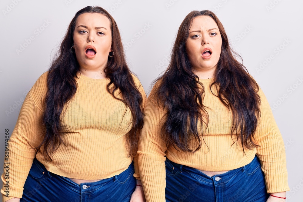 Young plus size twins wearing casual clothes in shock face, looking skeptical and sarcastic, surprised with open mouth Young plus size twins wearing casual clothes in shock face, looking skeptical and sarcastic, surprised with open mouth