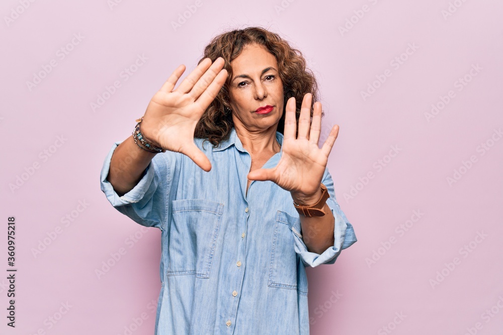Middle age beautiful woman wearing casual denim shirt standing over pink background doing frame using hands palms and fingers, camera perspective Middle age beautiful woman wearing casual denim shirt standing over pink background doing frame using hands palms and fingers, camera perspective
