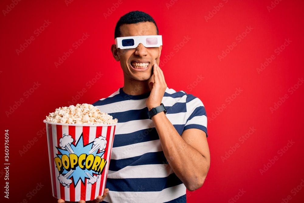 Φωτογραφία Young handsome african american man watching movie using 3d glasses eating popcorns touching mouth with hand with painful expression because of toothache or dental illness on teeth
