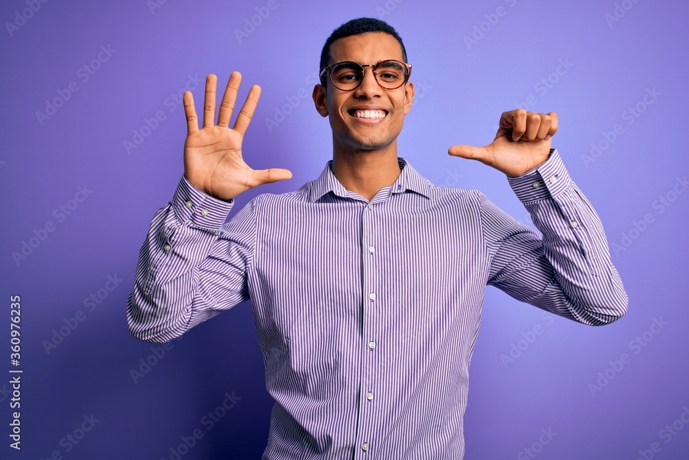 Naklejka premium Handsome african american man wearing striped shirt and glasses over purple background showing and pointing up with fingers number six while smiling confident and happy.