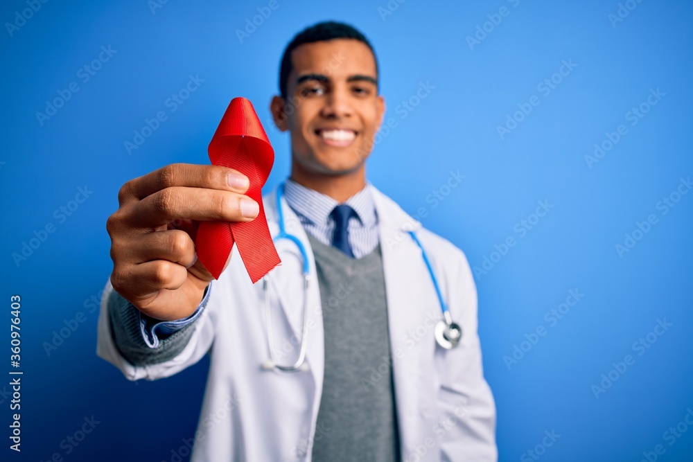 Young handsome african american doctor man holding red HIV ribbon symbol with a happy face standing and smiling with a confident smile showing teeth Young handsome african american doctor man holding red HIV ribbon symbol with a happy face standing and smiling with a confident smile showing teeth