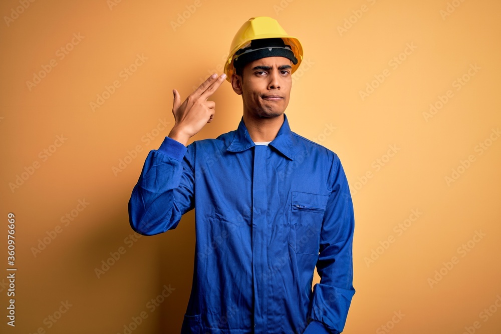 Young handsome african american worker man wearing blue uniform and security helmet Shooting and killing oneself pointing hand and fingers to head like gun, suicide gesture.
