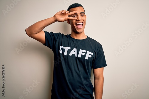 Young handsome african american worker man wearing staff uniform over white background Doing peace symbol with fingers over face, smiling cheerful showing victory