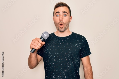 Young handsome singer man with blue eyes singing using microphone over white background scared in shock with a surprise face, afraid and excited with fear expression