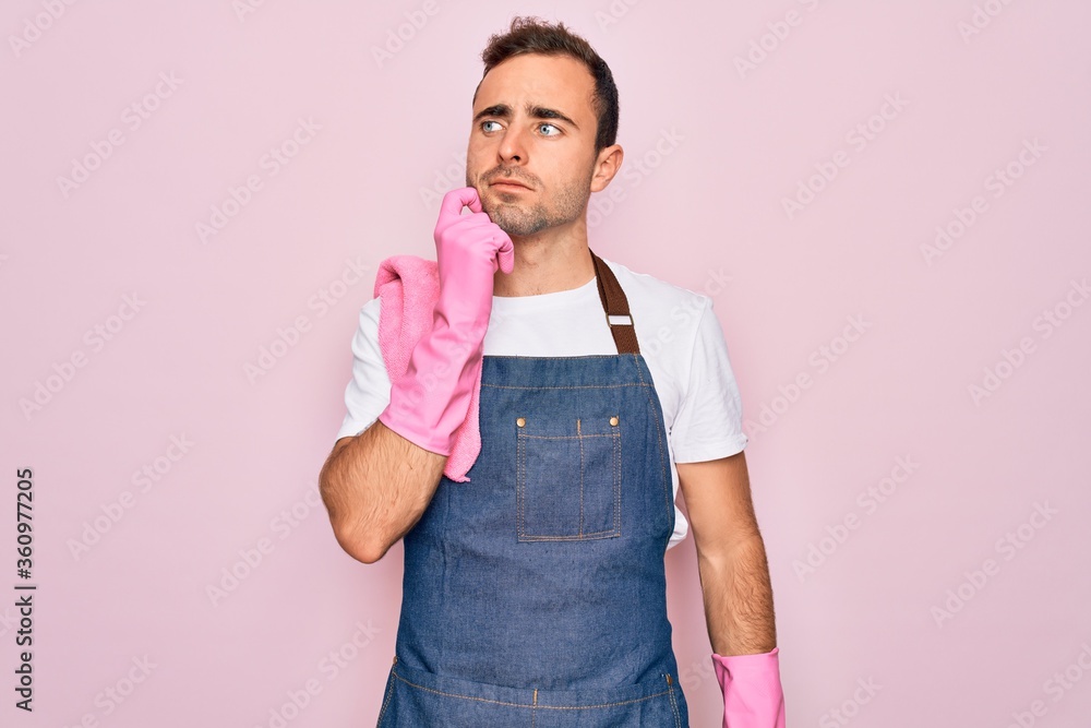 Young cleaner man with blue eyes cleaning wearing apron and gloves over pink background with hand on chin thinking about question, pensive expression. Smiling with thoughtful face. Doubt concept. Young cleaner man with blue eyes cleaning wearing apron and gloves over pink background with hand on chin thinking about question, pensive expression. Smiling with thoughtful face. Doubt concept.