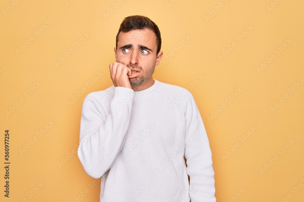 Young handsome man with blue eyes wearing casual sweater standing over yellow background looking stressed and nervous with hands on mouth biting nails. Anxiety problem. Young handsome man with blue eyes wearing casual sweater standing over yellow background looking stressed and nervous with hands on mouth biting nails. Anxiety problem.