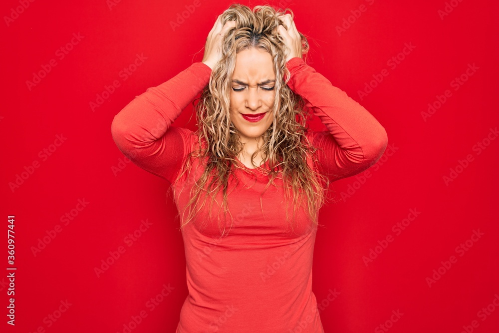 Young beautiful blonde woman wearing red casual t-shirt standing over isolated background suffering from headache desperate and stressed because pain and migraine. Hands on head. Young beautiful blonde woman wearing red casual t-shirt standing over isolated background suffering from headache desperate and stressed because pain and migraine. Hands on head.