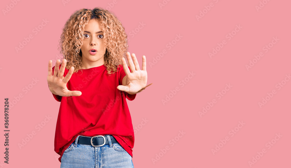 Young blonde woman with curly hair wearing casual red tshirt doing stop gesture with hands palms, angry and frustration expression Young blonde woman with curly hair wearing casual red tshirt doing stop gesture with hands palms, angry and frustration expression