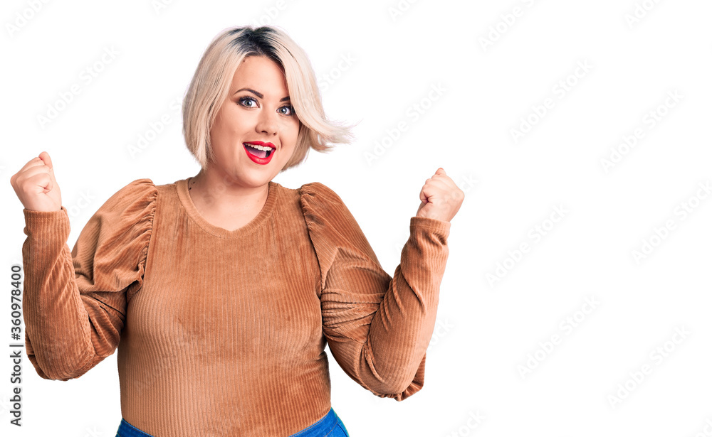 Young blonde plus size woman wearing casual sweater celebrating surprised and amazed for success with arms raised and open eyes. winner concept. Young blonde plus size woman wearing casual sweater celebrating surprised and amazed for success with arms raised and open eyes. winner concept.