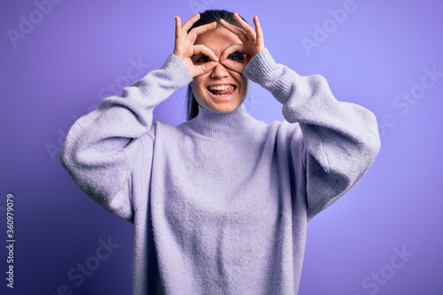 Young beautiful woman with blue eyes wearing casual turtleneck sweater over pink background doing ok gesture like binoculars sticking tongue out, eyes looking through fingers. Crazy expression. © Krakenimages.com