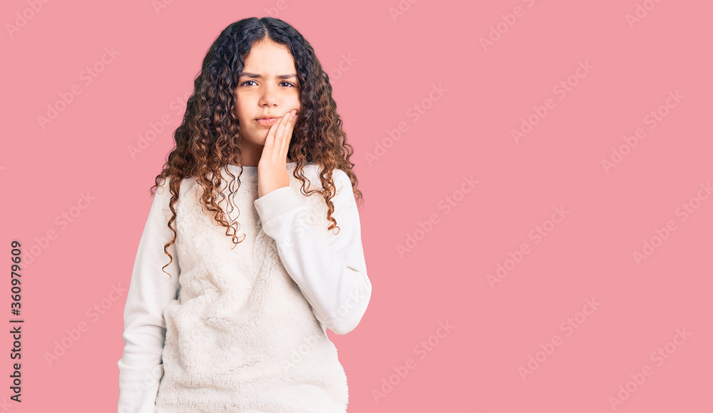 Beautiful kid girl with curly hair wearing casual clothes touching mouth with hand with painful expression because of toothache or dental illness on teeth. dentist