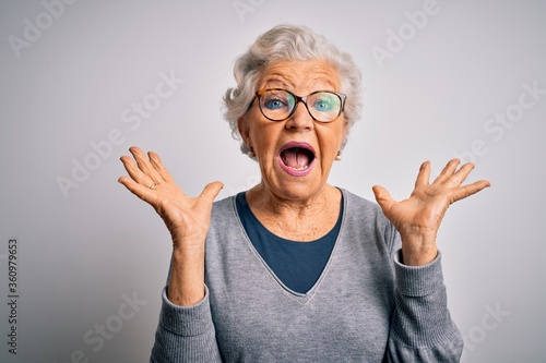 Senior beautiful grey-haired woman wearing casual sweater and glasses over white background celebrating crazy and amazed for success with arms raised and open eyes screaming excited. Winner concept