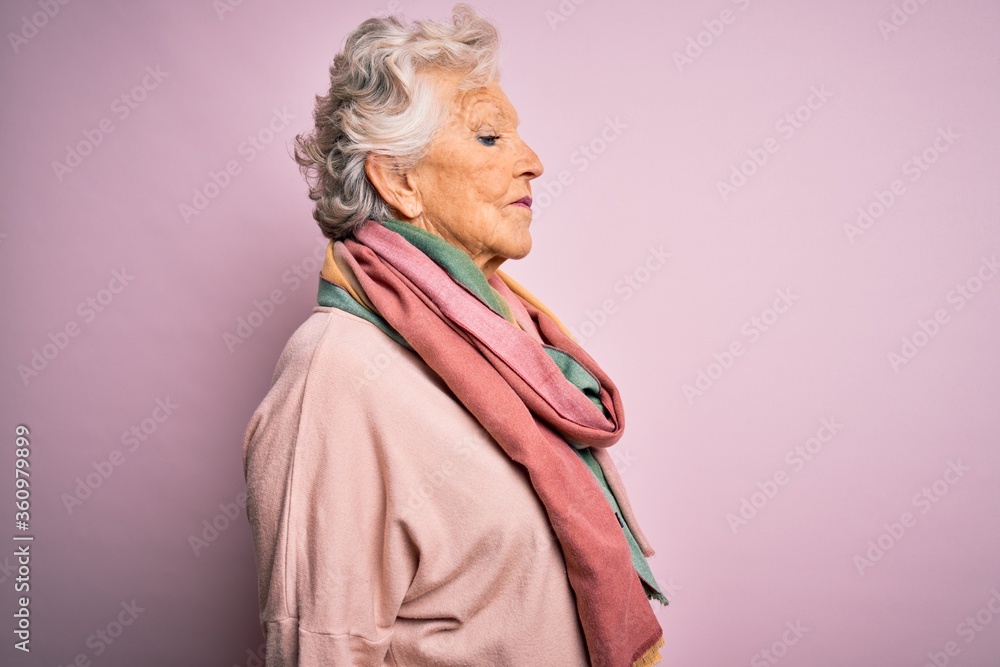 Senior beautiful grey-haired woman wearing casual sweater and scarf over pink background looking to side, relax profile pose with natural face with confident smile.