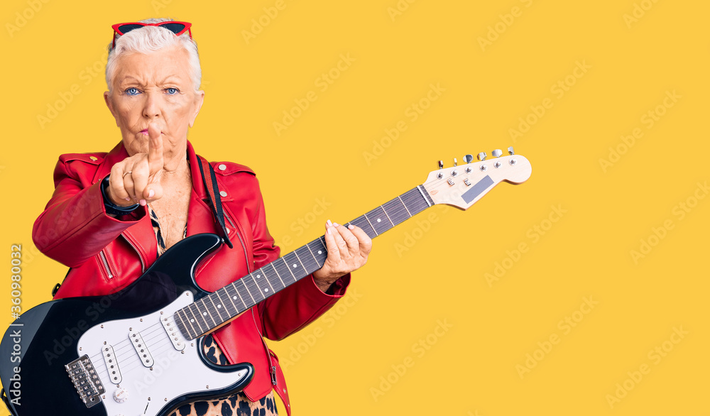 Senior beautiful woman with blue eyes and grey hair wearing a modern look playing electric guitar pointing with finger up and angry expression, showing no gesture