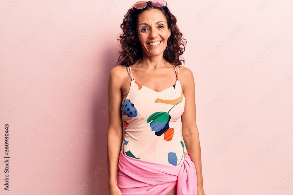 Obraz premium Middle age beautiful woman wearing swimwear and sunglasses looking positive and happy standing and smiling with a confident smile showing teeth