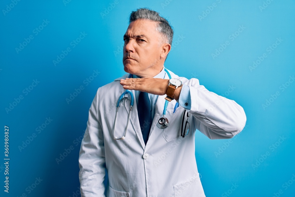 Middle age handsome grey-haired doctor man wearing coat and blue stethoscope cutting throat with hand as knife, threaten aggression with furious violence Middle age handsome grey-haired doctor man wearing coat and blue stethoscope cutting throat with hand as knife, threaten aggression with furious violence