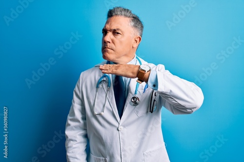 Middle age handsome grey-haired doctor man wearing coat and blue stethoscope cutting throat with hand as knife, threaten aggression with furious violence