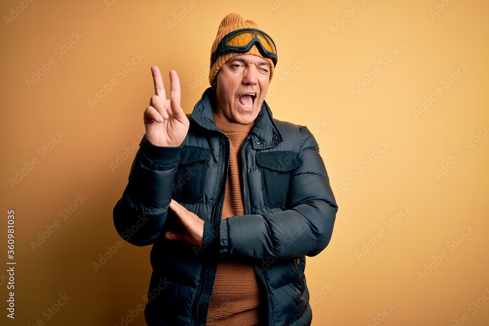 Middle age handsome grey-haired skier man on vacation wearing ski goggles smiling with happy face winking at the camera doing victory sign. Number two. Middle age handsome grey-haired skier man on vacation wearing ski goggles smiling with happy face winking at the camera doing victory sign. Number two.