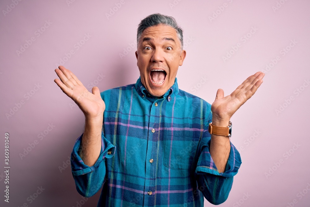 Naklejka premium Middle age handsome grey-haired man wearing casual shirt over isolated pink background celebrating crazy and amazed for success with arms raised and open eyes screaming excited. Winner concept