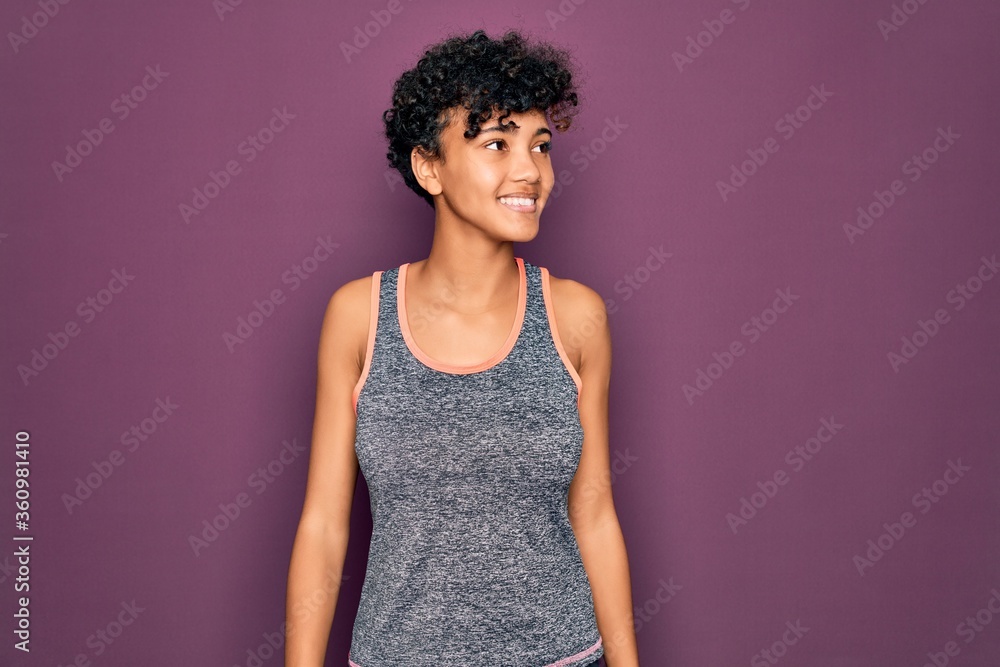 Young beautiful african american afro sportswoman doing exercise wearing sportswear looking away to side with smile on face, natural expression. Laughing confident. Young beautiful african american afro sportswoman doing exercise wearing sportswear looking away to side with smile on face, natural expression. Laughing confident.