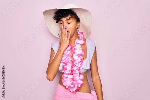 Young beautiful african american tourist woman wearing bikini and hawaiian lei flowers bored yawning tired covering mouth with hand. Restless and sleepiness.