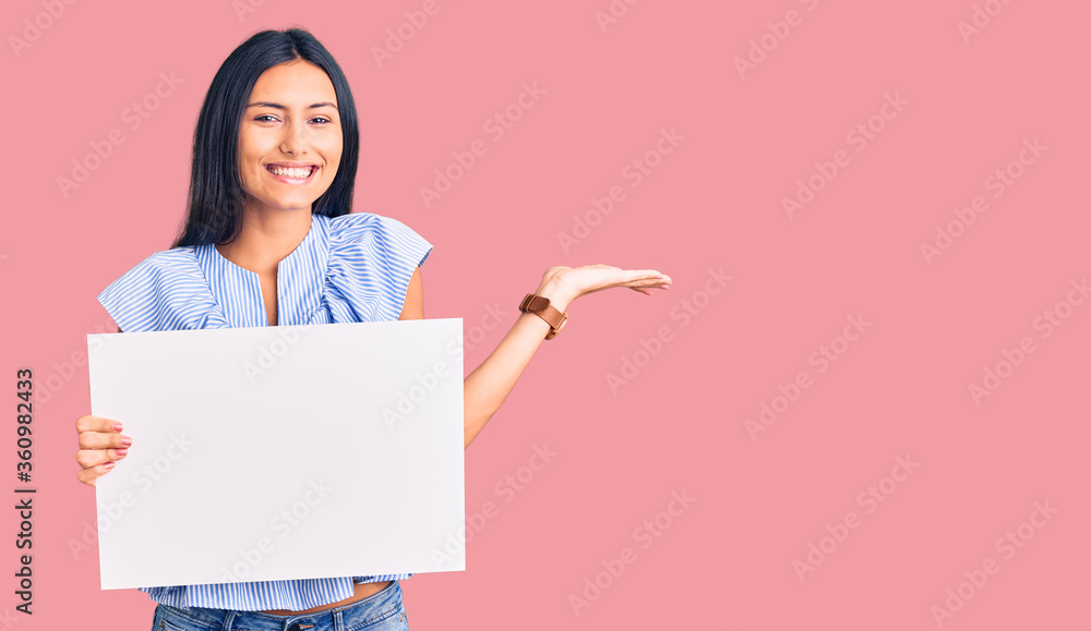 Young beautiful latin girl holding blank empty banner celebrating victory with happy smile and winner expression with raised hands Young beautiful latin girl holding blank empty banner celebrating victory with happy smile and winner expression with raised hands