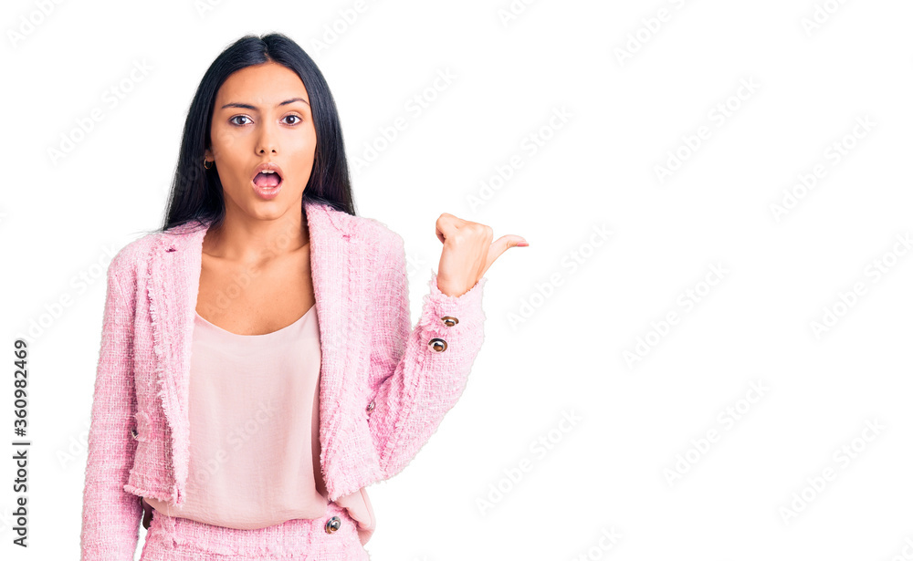 Young beautiful latin girl wearing business clothes surprised pointing with hand finger to the side, open mouth amazed expression. Young beautiful latin girl wearing business clothes surprised pointing with hand finger to the side, open mouth amazed expression.