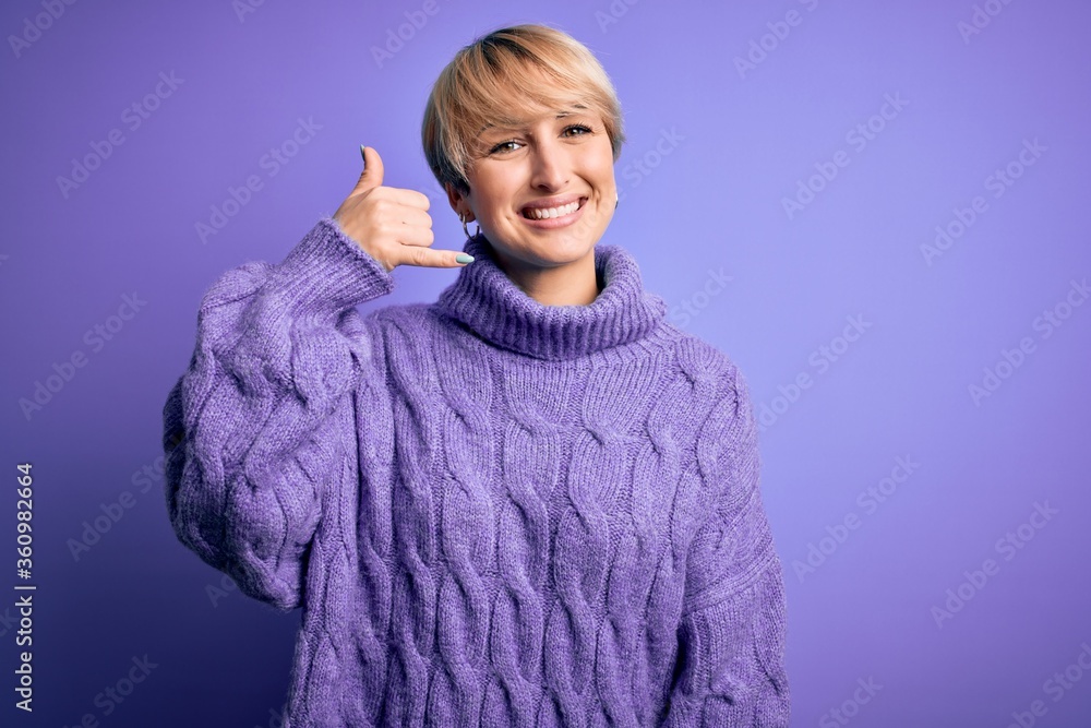 Young blonde woman with short hair wearing winter turtleneck sweater over purple background smiling doing phone gesture with hand and fingers like talking on the telephone. Communicating concepts. Young blonde woman with short hair wearing winter turtleneck sweater over purple background smiling doing phone gesture with hand and fingers like talking on the telephone. Communicating concepts.