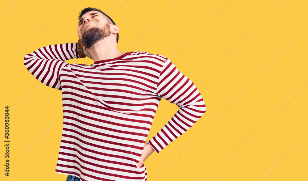 Young handsome man wearing striped sweater suffering of neck ache injury, touching neck with hand, muscular pain Young handsome man wearing striped sweater suffering of neck ache injury, touching neck with hand, muscular pain