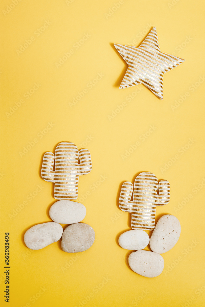 Fototapeta premium Summer composition with golden striped cactus on round sea pebbles and bright star in desert on yellow background. Creative summer concept.