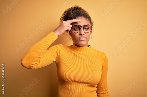 Young beautiful african american girl wearing sweater and glasses over yellow background worried and stressed about a problem with hand on forehead, nervous and anxious for crisis © Krakenimages.com