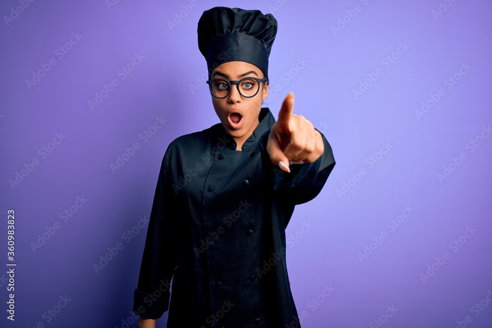 Young african american chef girl wearing cooker uniform and hat over purple background Pointing with finger surprised ahead, open mouth amazed expression, something on the front Young african american chef girl wearing cooker uniform and hat over purple background Pointing with finger surprised ahead, open mouth amazed expression, something on the front