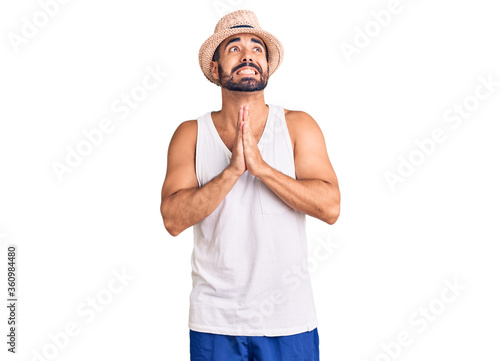 Photos Young hispanic man wearing casual summer hat begging and praying with hands together with hope expression on face very emotional and worried