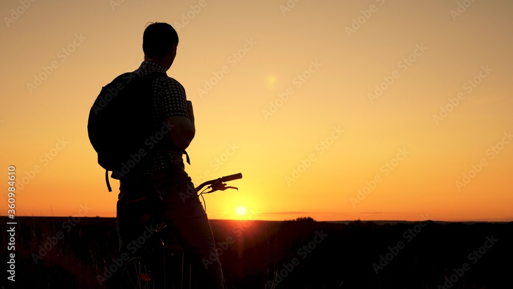 A free traveler travels with a bicycle at sunset. concept of adventure and travel. lonely cyclist resting in park. Hiker healthy young man rides bicycle to edge of the hill, enjoying nature and sun.