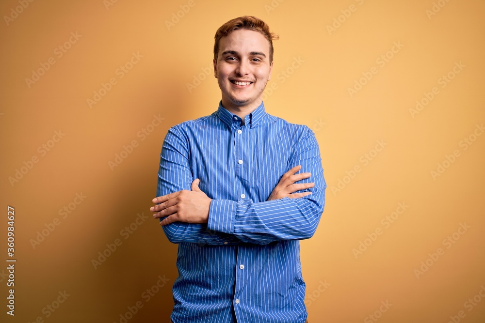 Young handsome redhead man wearing casual striped shirt over isolated yellow background happy face smiling with crossed arms looking at the camera. Positive person. Young handsome redhead man wearing casual striped shirt over isolated yellow background happy face smiling with crossed arms looking at the camera. Positive person.