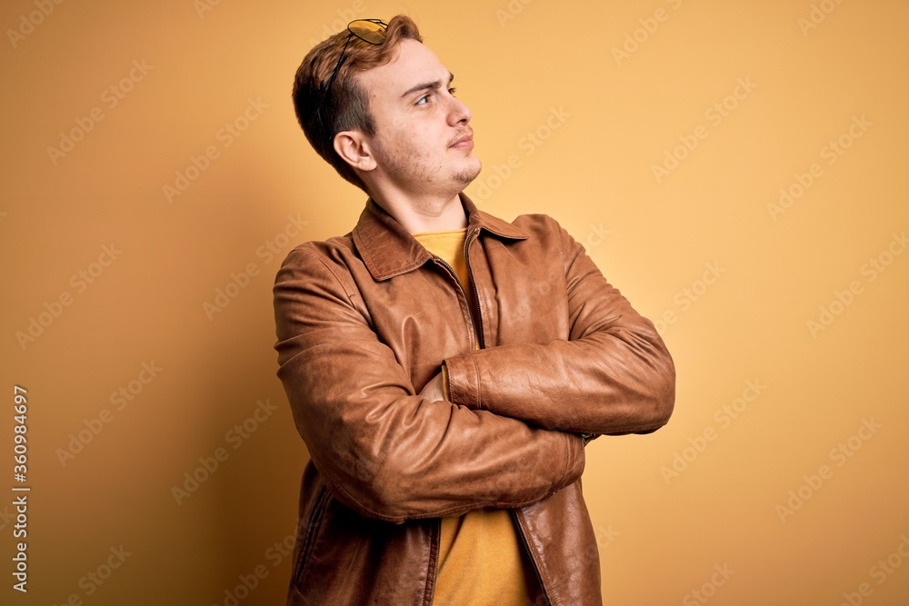 Obraz premium Young handsome redhead man wearing casual leather jacket over isolated yellow background looking to the side with arms crossed convinced and confident