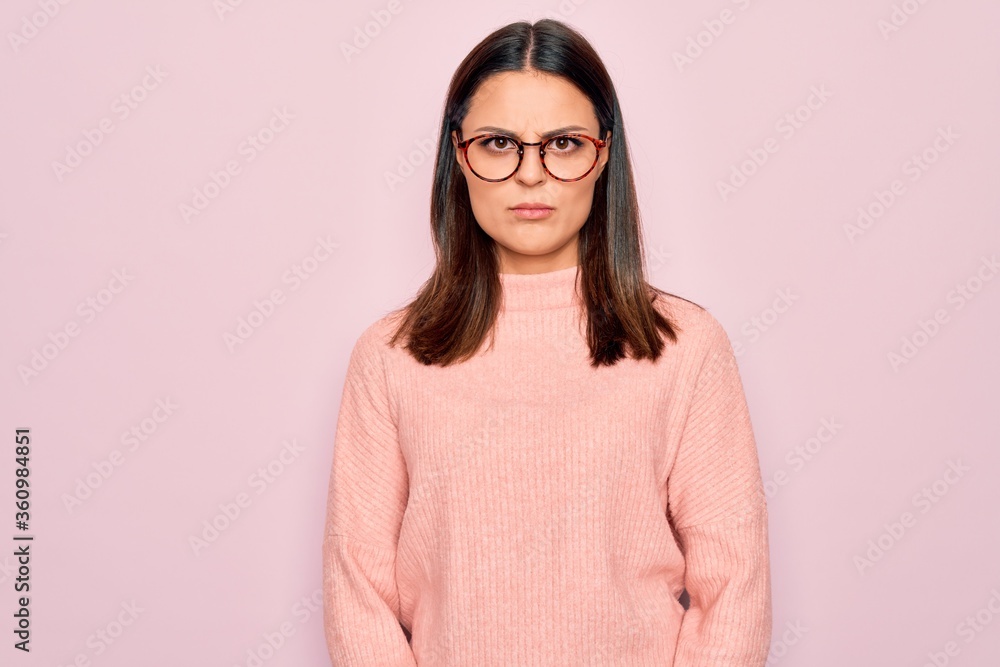 Young beautiful brunette woman wearing casual sweater and glasses over pink background skeptic and nervous, frowning upset because of problem. Negative person.