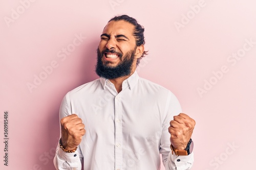 Young arab man wearing casual clothes very happy and excited doing winner gesture with arms raised, smiling and screaming for success. celebration concept.