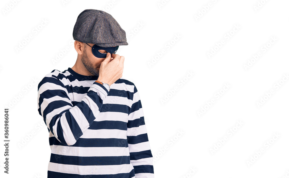 Young handsome man wearing burglar mask tired rubbing nose and eyes feeling fatigue and headache. stress and frustration concept. Young handsome man wearing burglar mask tired rubbing nose and eyes feeling fatigue and headache. stress and frustration concept.